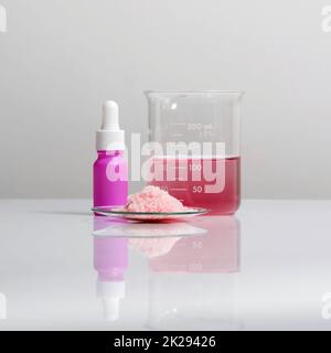 Produits chimiques pour soins de beauté sur table de laboratoire blanche. Produits chimiques à paillettes roses dans le verre de surveillance chimique placez-les à côté du flacon de sérum avec compte-gouttes et rasinine liquide époxy rouge dans le bécher. Banque D'Images