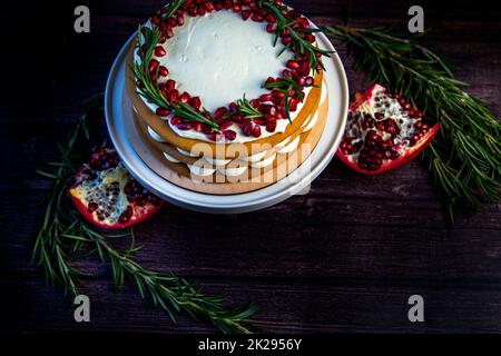 Le gâteau à la crème blanche et aux gâteaux bruns au miel se trouve sur un support blanc, décoré de grenade et de romarin, contre un arbre sombre Banque D'Images