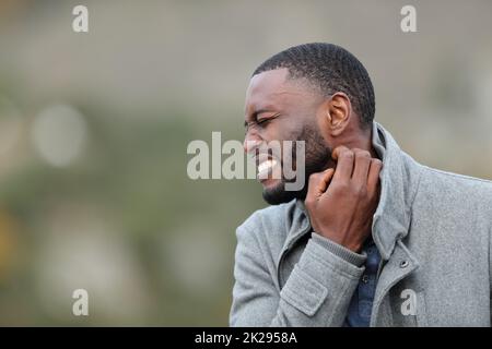 Homme stressé avec peau noire rayant le cou en hiver Banque D'Images