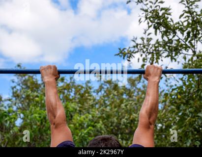 Les mains sur la barre de près. L'homme tire lui-même sur la barre. Faire du sport dans l'air frais. Barre horizontale. Banque D'Images
