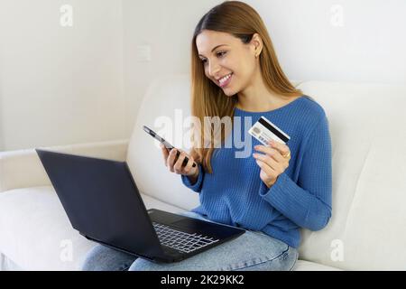 Femme brésilienne tenant une carte de crédit et un smartphone utilisant un ordinateur portable pour faire des achats en ligne à la maison. OTP, authentification à deux facteurs, pix et jeton pour le paiement en ligne. Banque D'Images