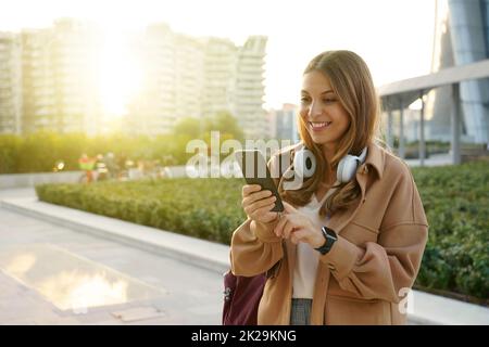 Jeune femme caucasienne utilisant un téléphone sur fond de ville moderne au coucher du soleil Banque D'Images