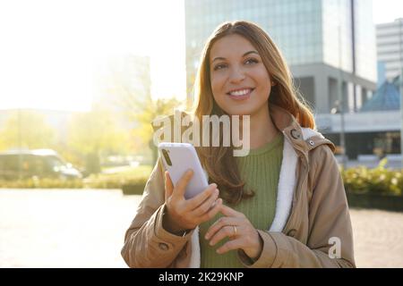 Belle fille souriante tenant son smartphone à l'extérieur au coucher du soleil Banque D'Images