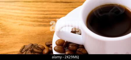 Une tasse de café sur une table en bois parmi des grains de café fraîchement torréfiés. Banque D'Images