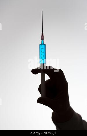 Silhouette de la main d'un médecin avec une seringue remplie de liquide bleu. Concept de vaccination. Banque D'Images