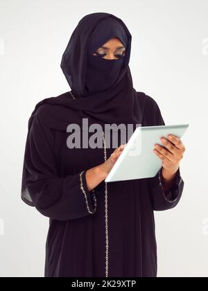 Axé sur ses e-mails. Photo en studio d'une femme dans une burqa à l'aide d'une tablette numérique. Banque D'Images