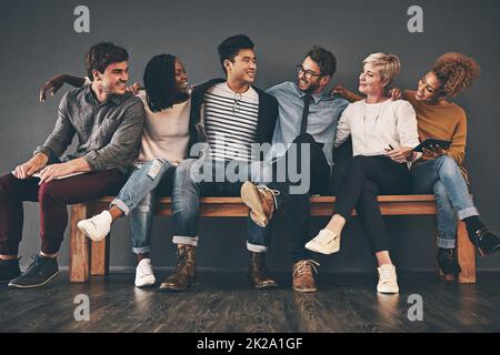 Collage sur le banc. Photo en studio d'un groupe diversifié d'employés créatifs s'embrassant les uns les autres sur un fond gris. Banque D'Images