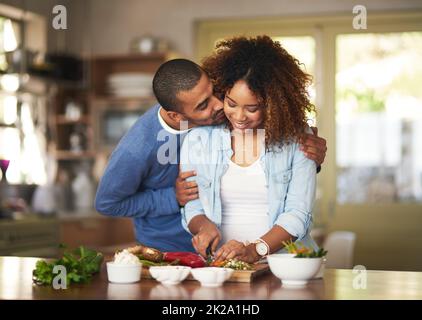 Le mariage sain est un mariage heureux. Photo d'un jeune homme embrassant sa femme pendant qu'elle prépare un repas sain à la maison. Banque D'Images