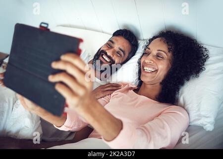 Réveillez-vous dans un monde sans fil. Photo d'un couple mature utilisant une tablette numérique tout en se relaxant ensemble dans le lit. Banque D'Images