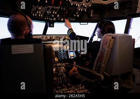 Female pilot assisting captain to takeoff and fly airplane, using buttons on dashboard command in pilot cockpit. Airliners flying plane jet with navigation windscreen and control panel. Stock Photo