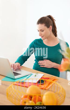 Se préparer à l'arrivée de son bébé par des recherches en ligne. Une femme enceinte utilisant son ordinateur portable à la maison Banque D'Images