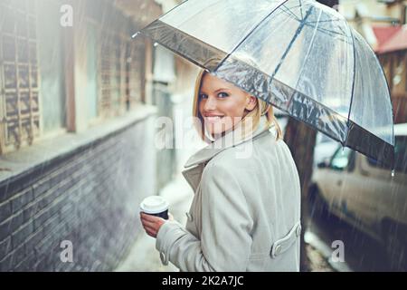 Réchauffer avec un café. Portrait arrière d'une jeune femme attrayante marchant sous la pluie avec un parapluie et un café. Banque D'Images