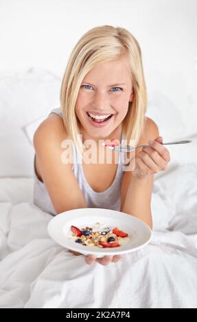 Petit déjeuner au lit. Une jeune femme attrayante mangeant son petit déjeuner au lit. Banque D'Images