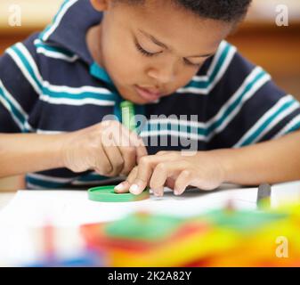 Son temps créatif. Avant l'école, un garçon afro-américain se concentrant sur ses dessins avec ses crayons et ses formes. Banque D'Images