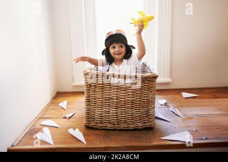 Laissez libre cours à votre imagination. Un petit garçon jouant avec des avions en peluche tout en étant assis dans un panier. Banque D'Images