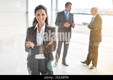 Ses a reçu le sourire d'une confiance suprême. Portrait court d'une femme d'affaires debout dans un hall avec ses collègues en arrière-plan. Banque D'Images