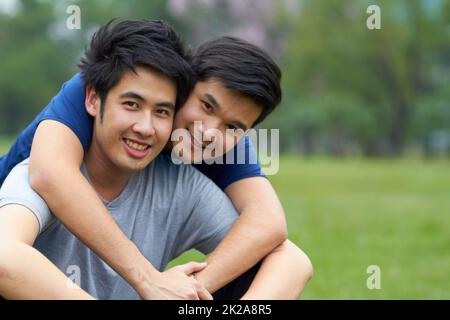 Vivre et aimer ensemble. Mignon jeune gay asiatique couple souriant ensemble tout en étant assis dans le parc. Banque D'Images