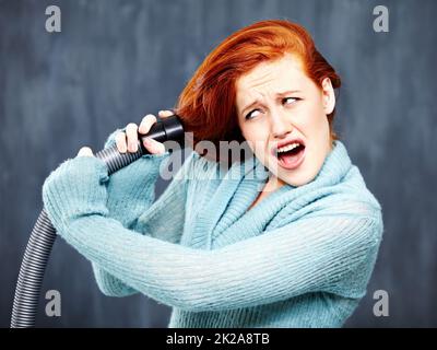 Ce n'est pas la meilleure façon de nettoyer vos cheveux. Une jeune tête rouge avec ses cheveux pris dans l'aspirateur. Banque D'Images