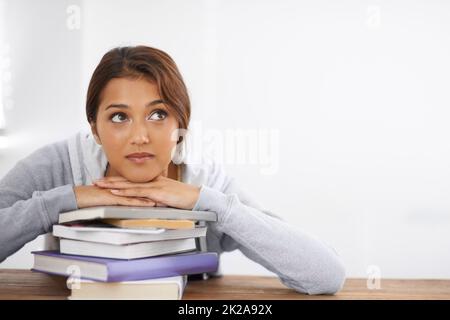 Penser à des solutions à un problème. Gros plan d'une étudiante attrayante penchée sur ses livres et regardant réfléchie. Banque D'Images