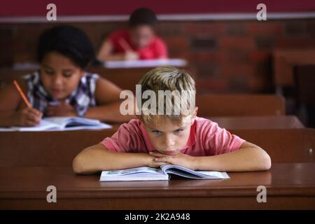 L'école suce. Un jeune garçon reposant sa tête sur les bras pendant qu'il est assis dans une salle de classe qui a l'air s'ennuyer. Banque D'Images