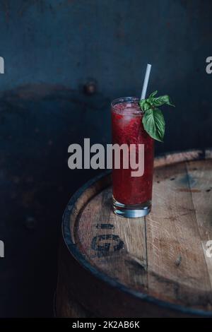 strawberry basil cocktail drink in tall Collins glass with drinking straw on wooden whiskey barrel Stock Photo