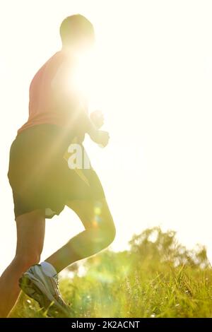 Courir au soleil. Vue arrière d'un jeune homme qui court en plein air sur un sentier de montagne. Banque D'Images