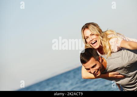 Toujours un rire quand étaient ensemble. Photo d'un beau jeune homme donnant à sa petite amie en riant un porcgyback à la plage. Banque D'Images