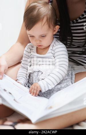 Shes déjà en train d'apprendre. Photo d'une petite fille mignonne assise sur son tour de mamans regardant à travers un livre d'images. Banque D'Images