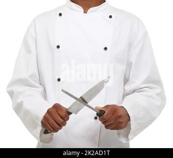 Outils du commerce. Un jeune chef aiguisant ses couteaux tout en étant isolé sur un fond blanc. Banque D'Images