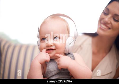 Ce que vous écoutez. Photo d'une adorable petite fille portant un casque tout en étant assise avec sa mère. Banque D'Images