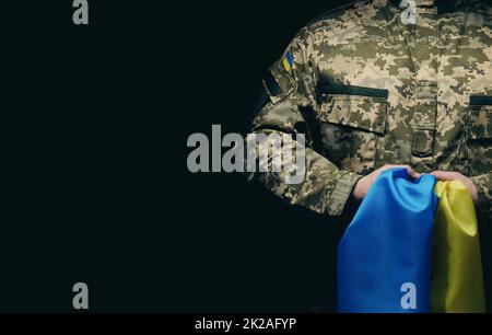 Le soldat des forces armées ukrainiennes est doté d'un drapeau bleu-jaune de l'Ukraine sur fond noir Banque D'Images