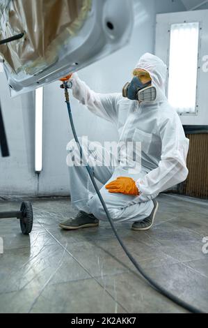 Technicien en vêtements de sécurité pulvérisant de la peinture pour voiture Banque D'Images