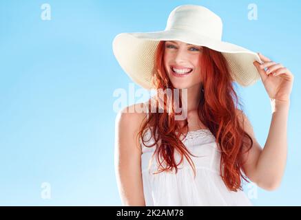 Les jours d'été sont ici. Une belle jeune femme à tête rouge portant un chapeau de soleil blanc tout en se tenant à l'extérieur. Banque D'Images