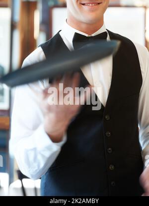 Je divertis mes clients. Un serveur tourne un plateau de service sur ses doigts dans un restaurant. Banque D'Images