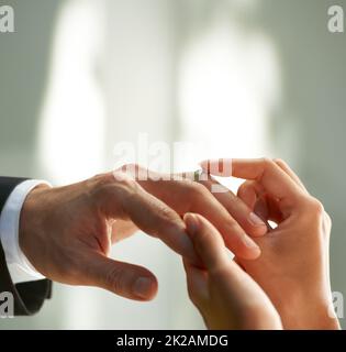 Exprimant leur amour et leur engagement. Vue rognée d'une mariée glissant un anneau sur son doigt de marié. Banque D'Images