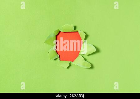 Un trou dans le papier vert avec des bords déchirés et un arrière-plan rouge à l'intérieur Banque D'Images