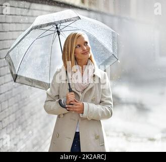 Une promenade sous la pluie. Photo d'une jeune femme marchant dans la rue avec un parapluie le jour des pluies. Banque D'Images