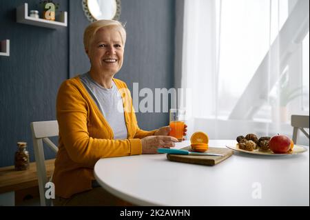 Femme souriante aux cheveux gris tenant un verre de jus Banque D'Images