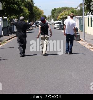 Nous courons ces rues. Photo de trois jeunes hommes marchant dans une rue de banlieue. Banque D'Images