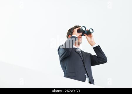 Homme d'affaires visionnaire. Vue à angle bas d'un beau homme d'affaires regardant à travers des jumelles. Banque D'Images