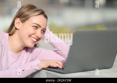 Un adolescent heureux en utilisant un ordinateur portable assis dans la rue Banque D'Images