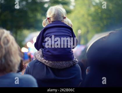 Meilleur siège dans la maison. Une petite fille assise sur ses épaules de pères à un événement en plein air. Banque D'Images