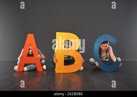 Où commence l'alphabétisation. Portrait studio d'un groupe diversifié d'enfants tenant des lettres de l'alphabet sur un fond gris. Banque D'Images