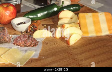 Salami au poivre sur plateau avec fromage anglais et irlandais, pommes en tranches et épices dans la cuisine rustique Banque D'Images