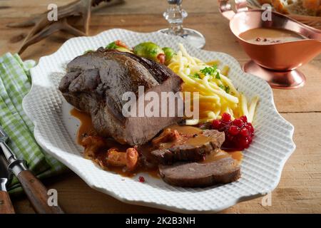 From above sliced delicious deer venison served with cranberry sauce on plate near potato fries and Brussels sprouts on wooden table during dinner Stock Photo