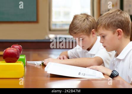 Axé sur leurs études. Deux jeunes écoliers assis en classe et lisant leur travail. Banque D'Images