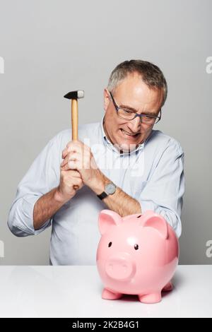 En réalisant des économies. Studio de tir d'un homme mûr sur le point de briser une porcgybank avec un marteau. Banque D'Images