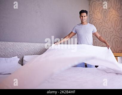 C'est parti pour la journée. Photo d'un jeune homme qui fait son lit le matin. Banque D'Images