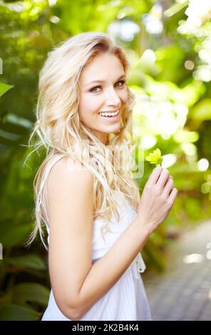 Beauté naturelle en été. Portrait d'une jolie jeune femme debout à l'extérieur tout en tenant une Marguerite. Banque D'Images