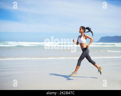 Faire avancer son jogging. Prise de vue en longueur d'une jeune femme qui court le long de la mer. Banque D'Images